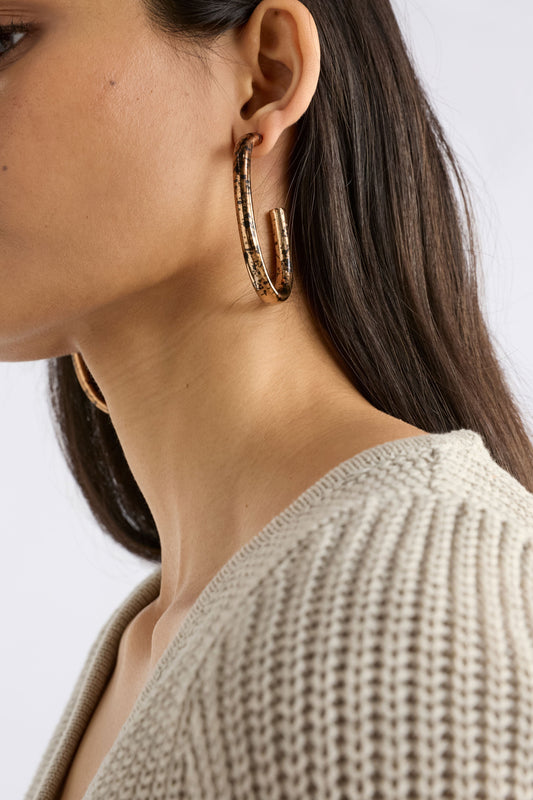 The Oban Large Hoop Earring features a bold open oval shape with a glistening metallic base and contrasting enamel splatter finish, on model | BRONZE